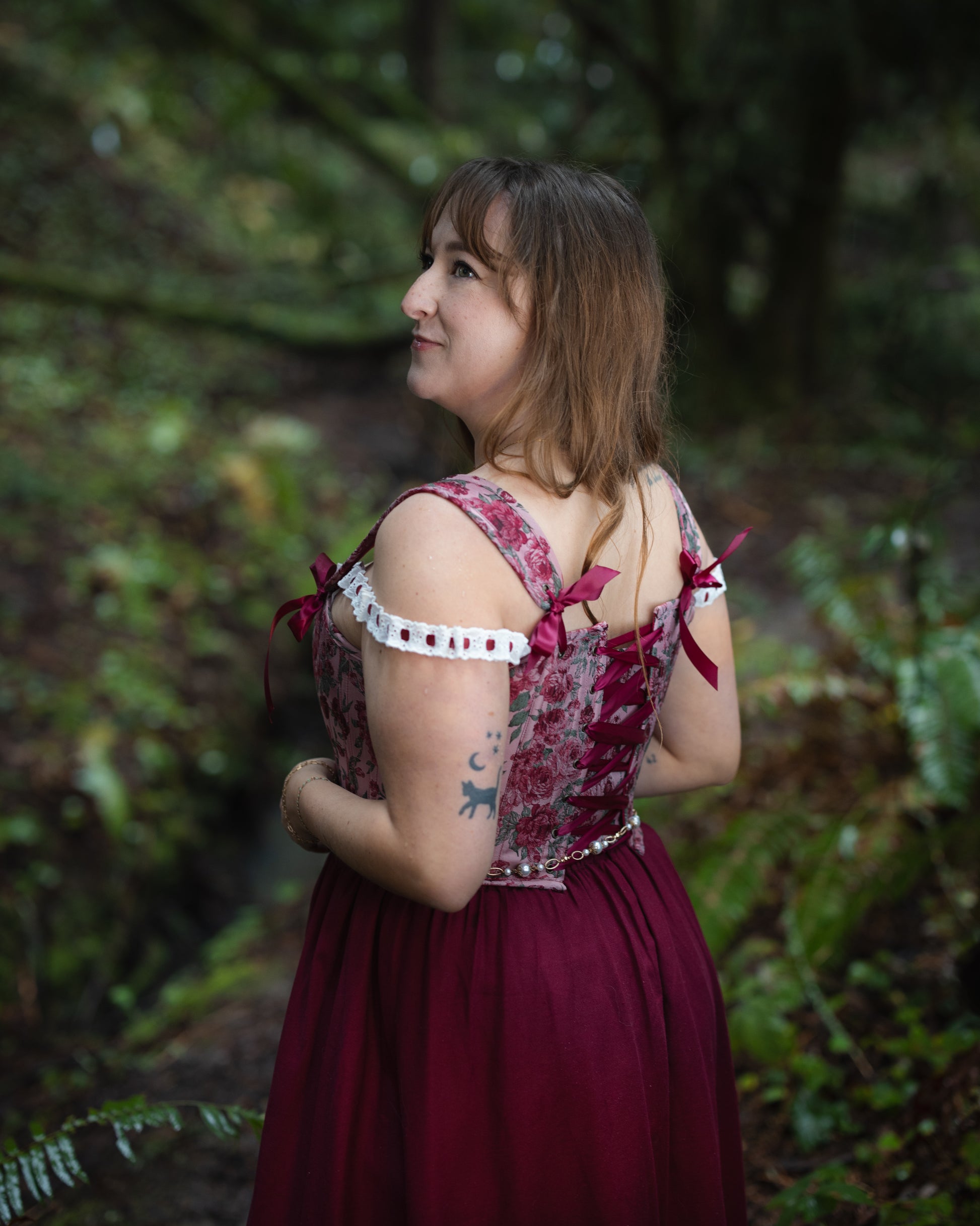 Woman wearing a Raspberry Rose Jacquard Corset with lace-up back and off-shoulder sleeves in an outdoor forest setting