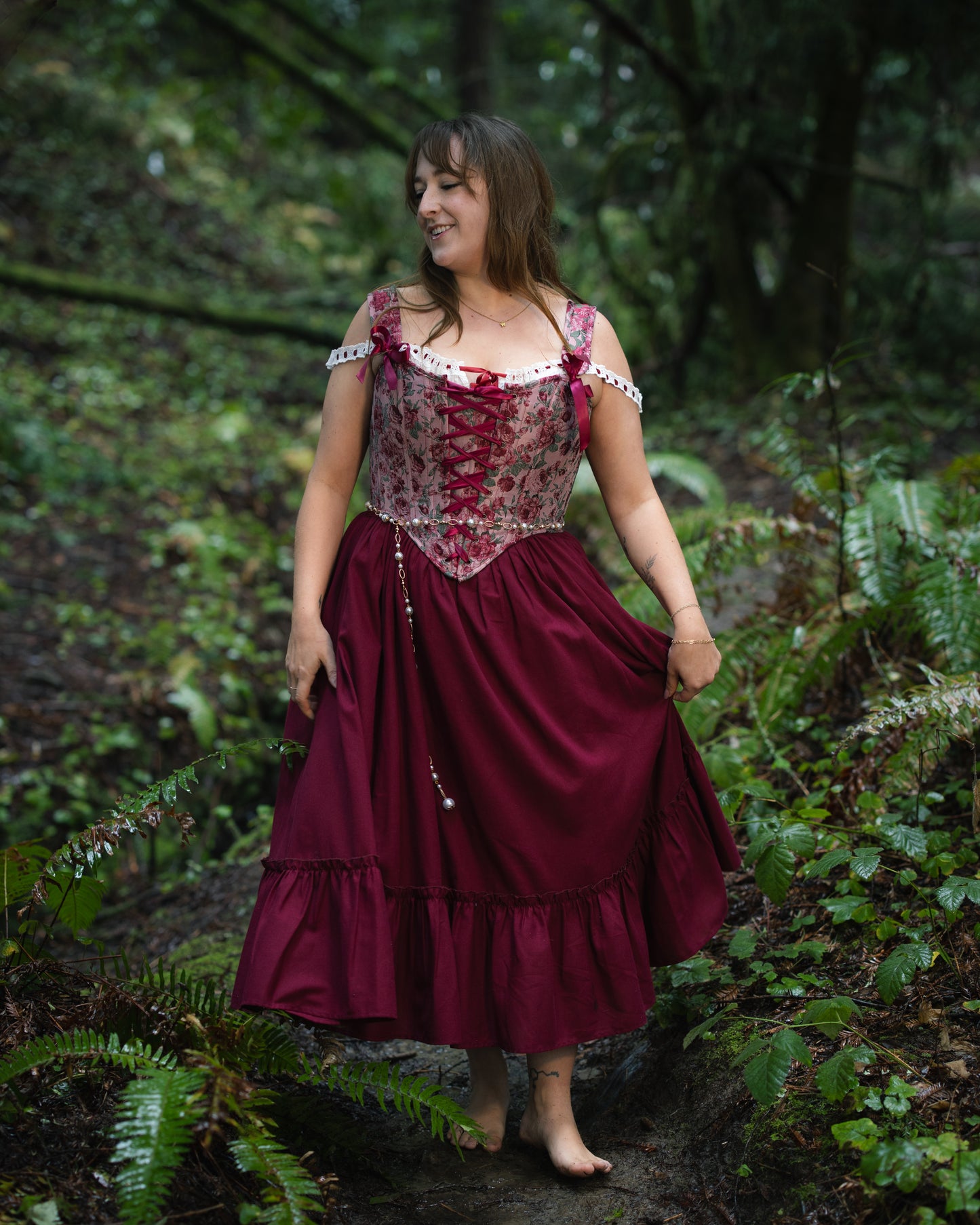 Woman standing barefoot in a forest wearing a flowing dress and Raspberry Rose Jacquard Corset with floral pattern and lace-up front