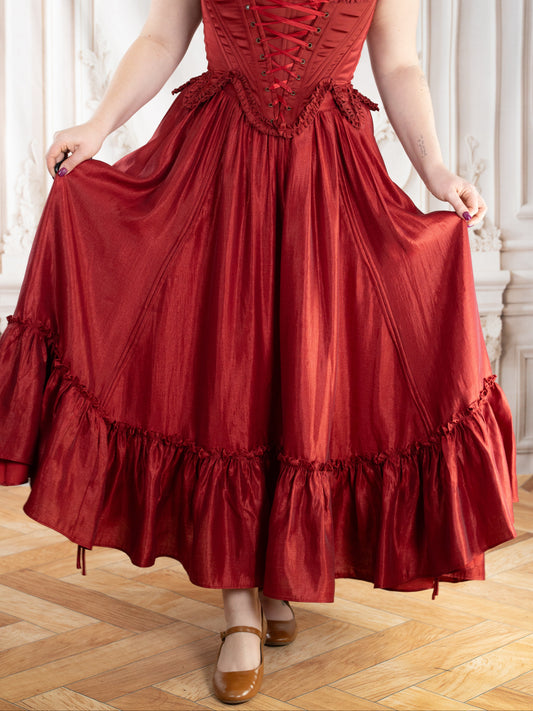 Woman wearing a dark red ruffle skirt with corset detailing and off-shoulder white blouse in an elegant room