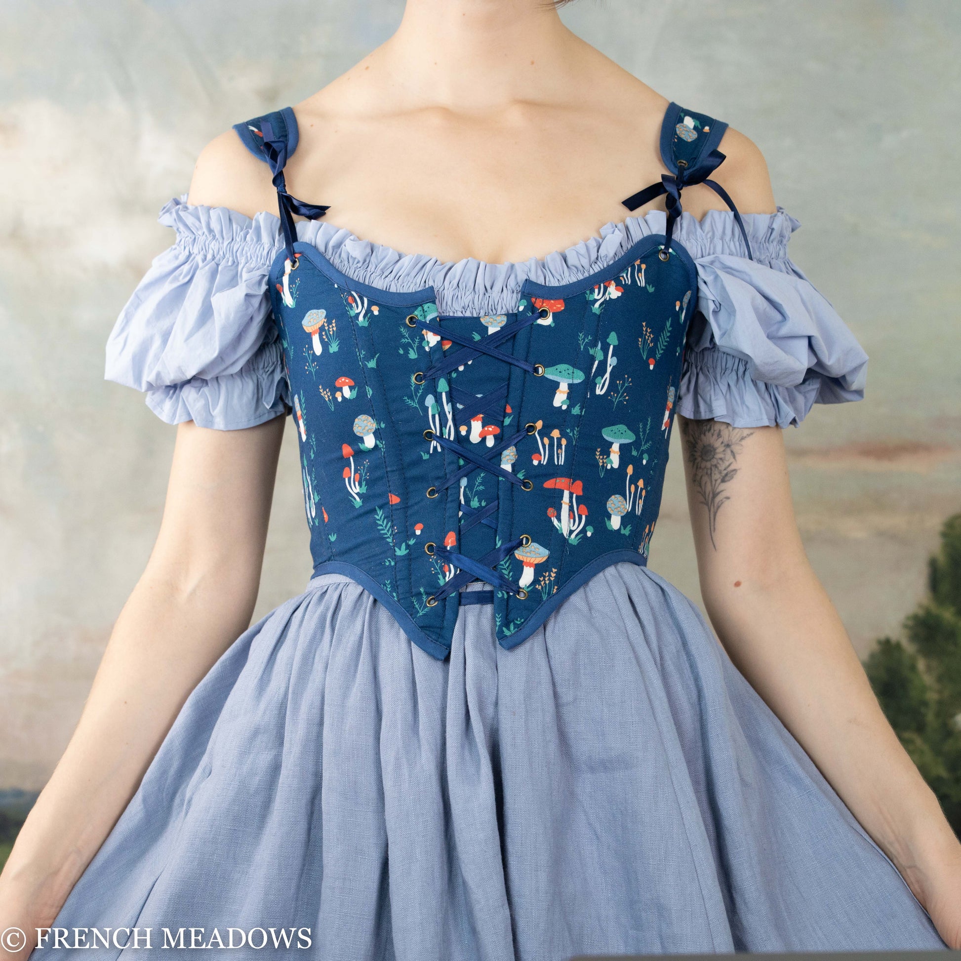 model wearing dark blue corset with mushrooms over a light blue puff sleeve dress and skirt