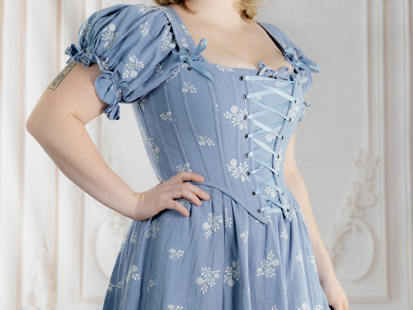 Woman wearing Regency Blue Floral Corset with puffed sleeves and delicate white floral pattern on blue fabric