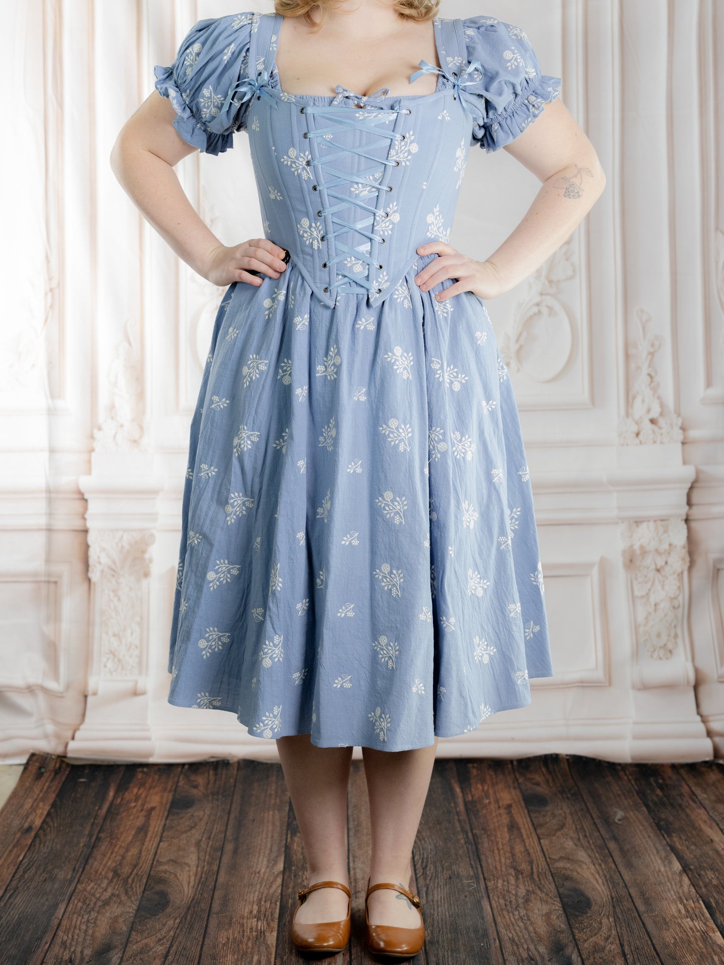 Woman wearing a Regency Blue Floral Corset with puff sleeves and delicate white floral patterns in a classic setting