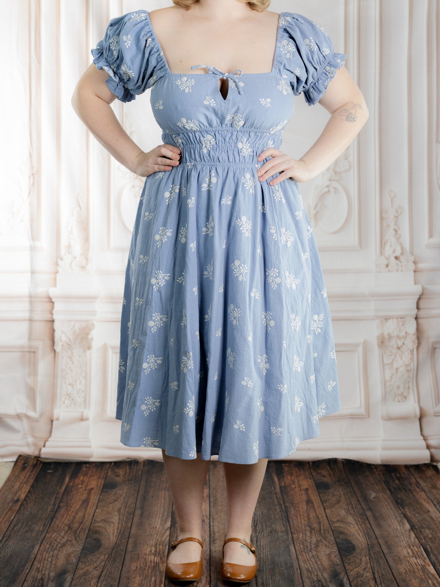 Woman wearing Regency Blue Floral Milkmaid Dress with puff sleeves and a square neckline in a vintage setting