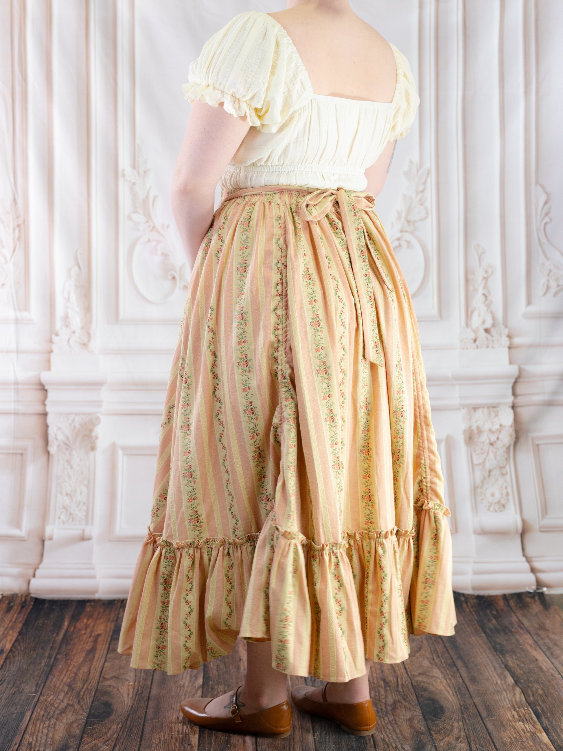 Back view of Rococo Pink Ruffle Skirt with floral stripes and adjustable tie worn with cream puff sleeve top