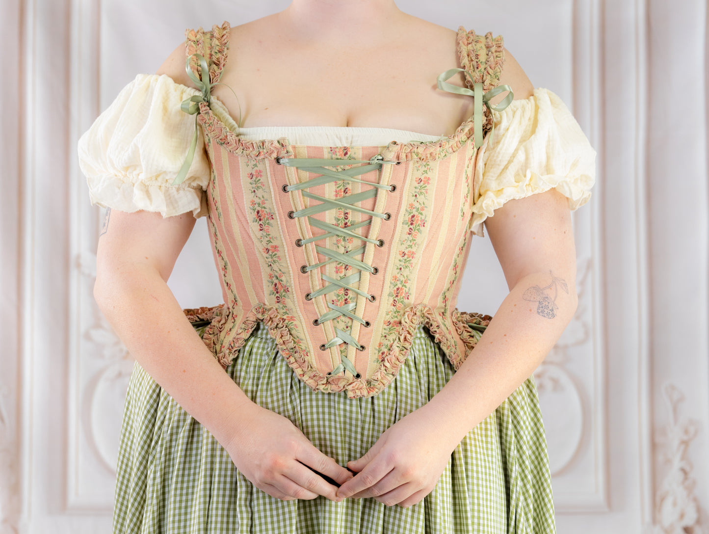 Person wearing Rococo Pink 18th Century Stays with pastel stripes and floral lace details over a cream blouse
