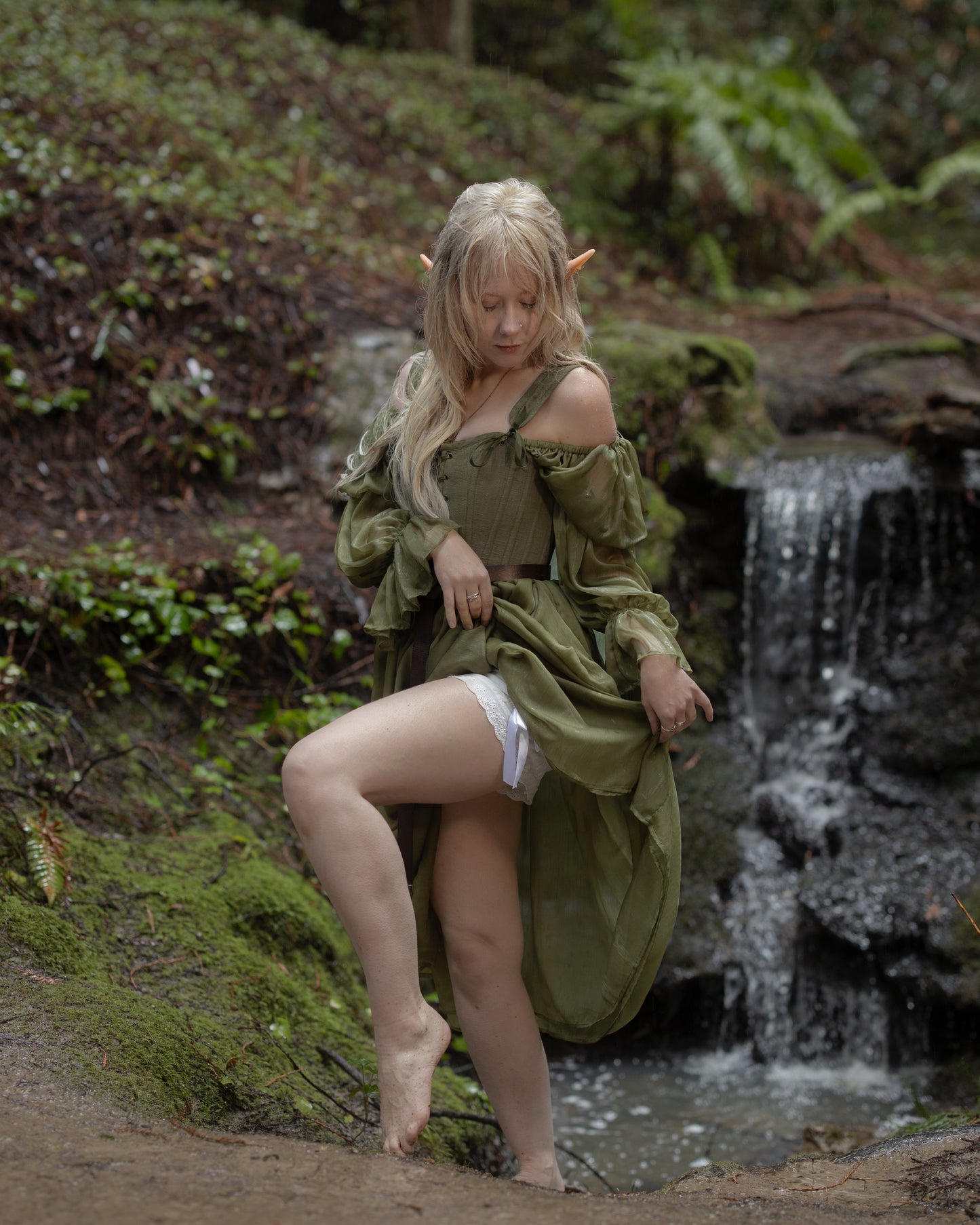 Woman in flowing green dress by waterfall revealing white lace Victorian Bloomers underneath