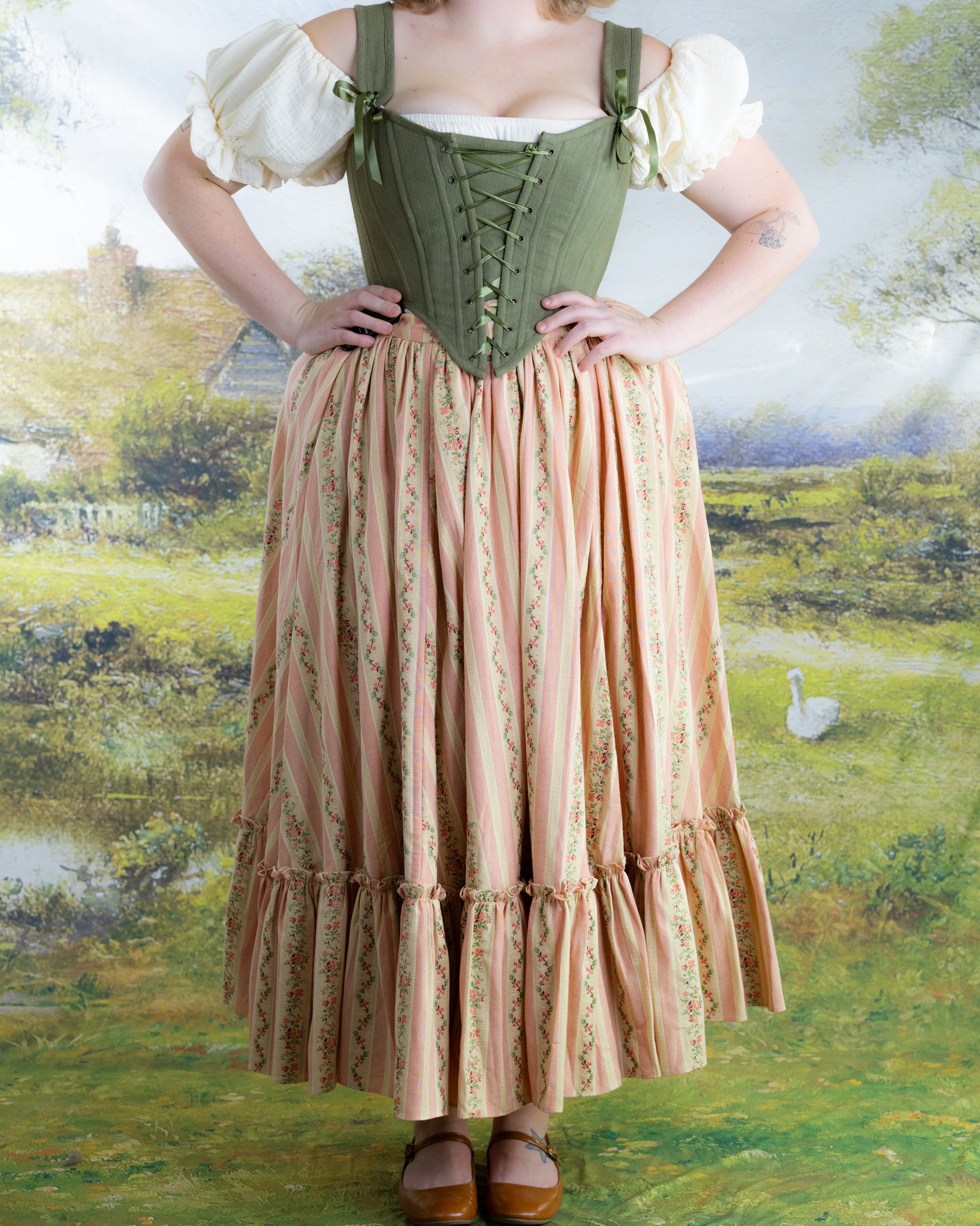 Woman wearing Rococo Pink Ruffle Skirt with floral stripes and ruffles styled with green corset and puffed sleeves