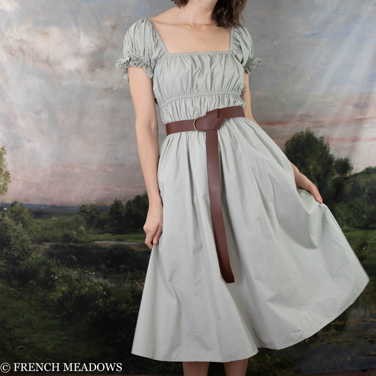 modeling wearing light pistachio colored dress with a leather O-ring belt belted at the waist and twirling to the side to show the volume of the skirt