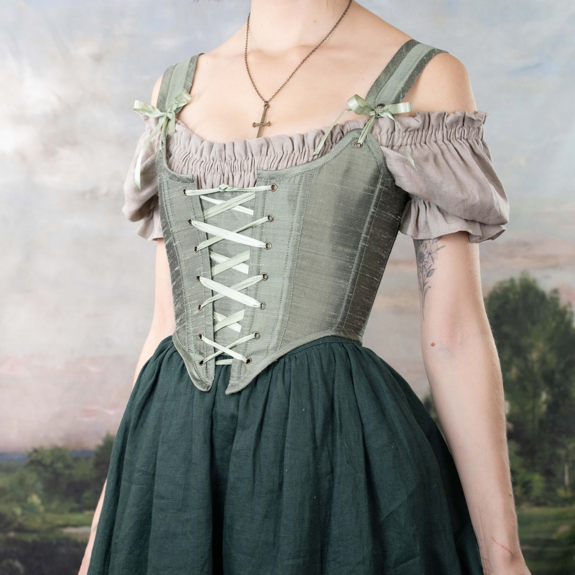 Woman wearing a Handmade Sage Green Silk Corset over puffed sleeves and a dark green skirt in a soft natural setting