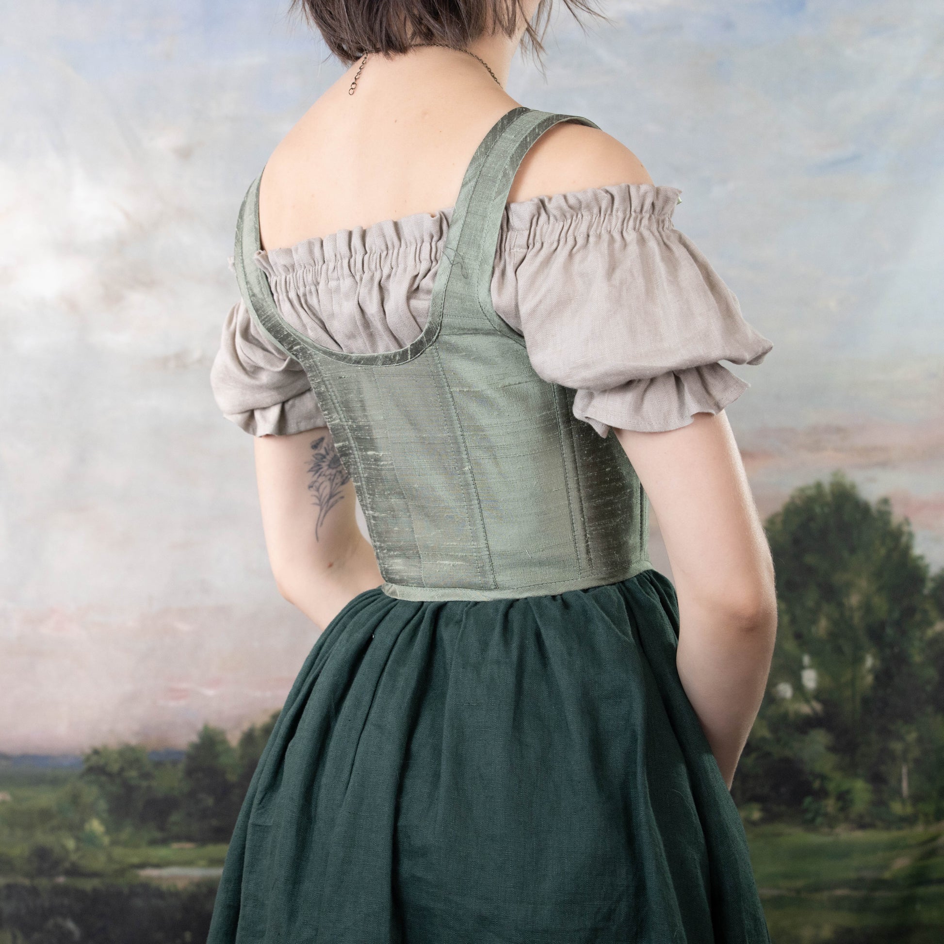 Back view of a person wearing a Handmade Sage Green Silk Corset over an off-shoulder blouse with a dark skirt.