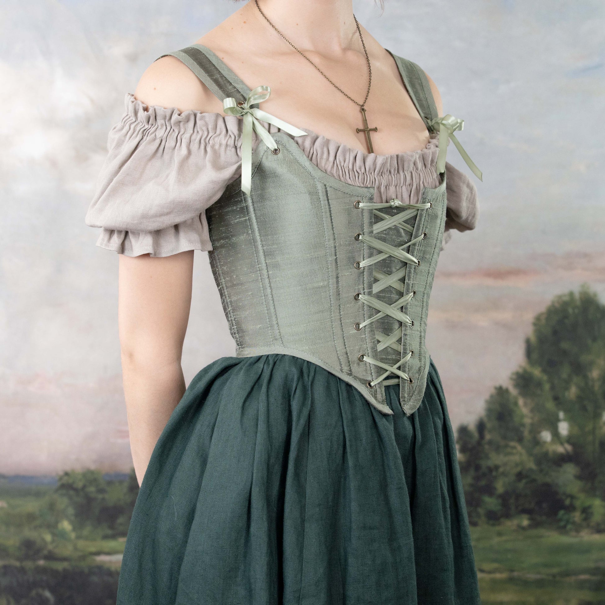 Handmade Sage Green Silk Corset with delicate lacing and subtle sheen worn over an off-shoulder blouse in a vintage style setting
