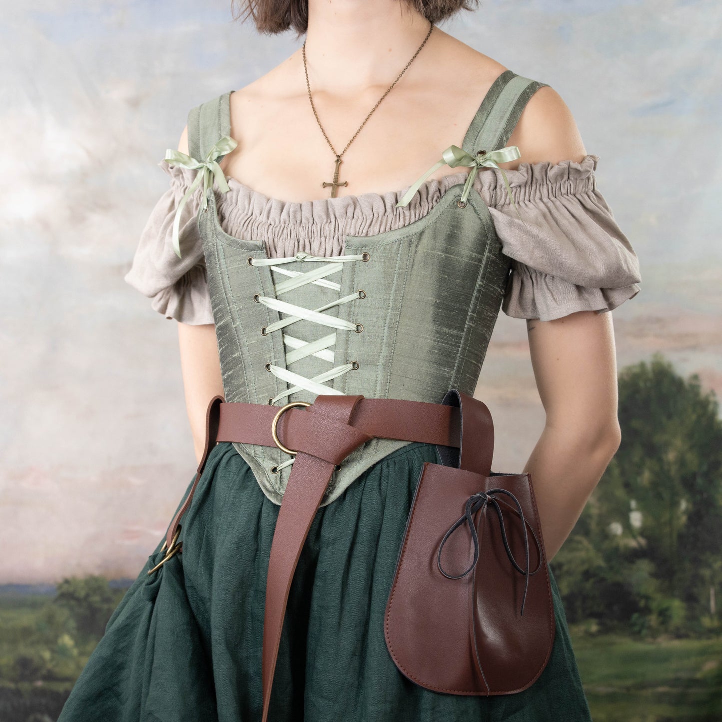 Woman wearing Handmade Sage Green Silk Corset with off-shoulder blouse, brown belt, and leather pouch outdoors
