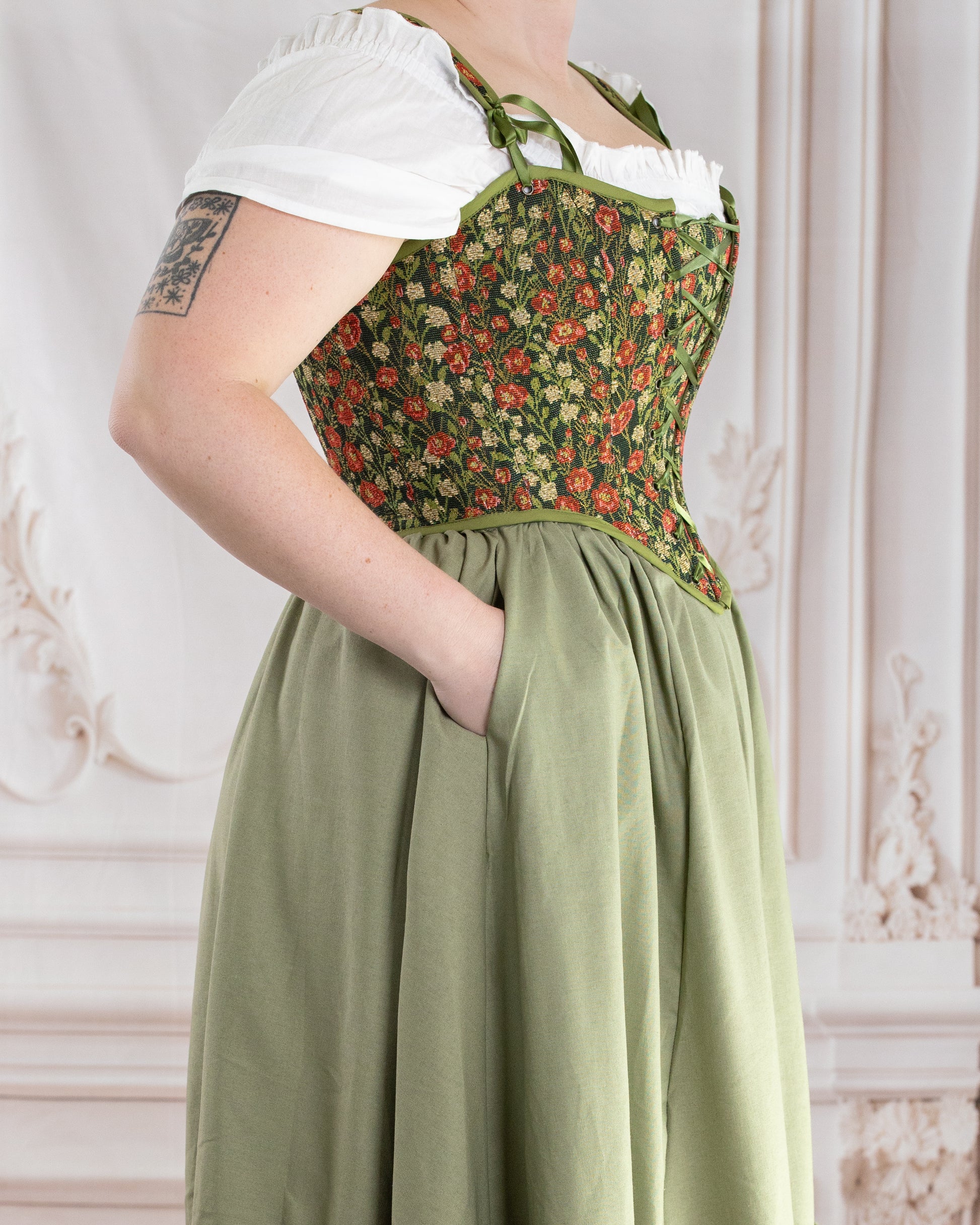 Side view of a person wearing a Sage Linen Ruffle Skirt with their hand in the pocket against a decorative background