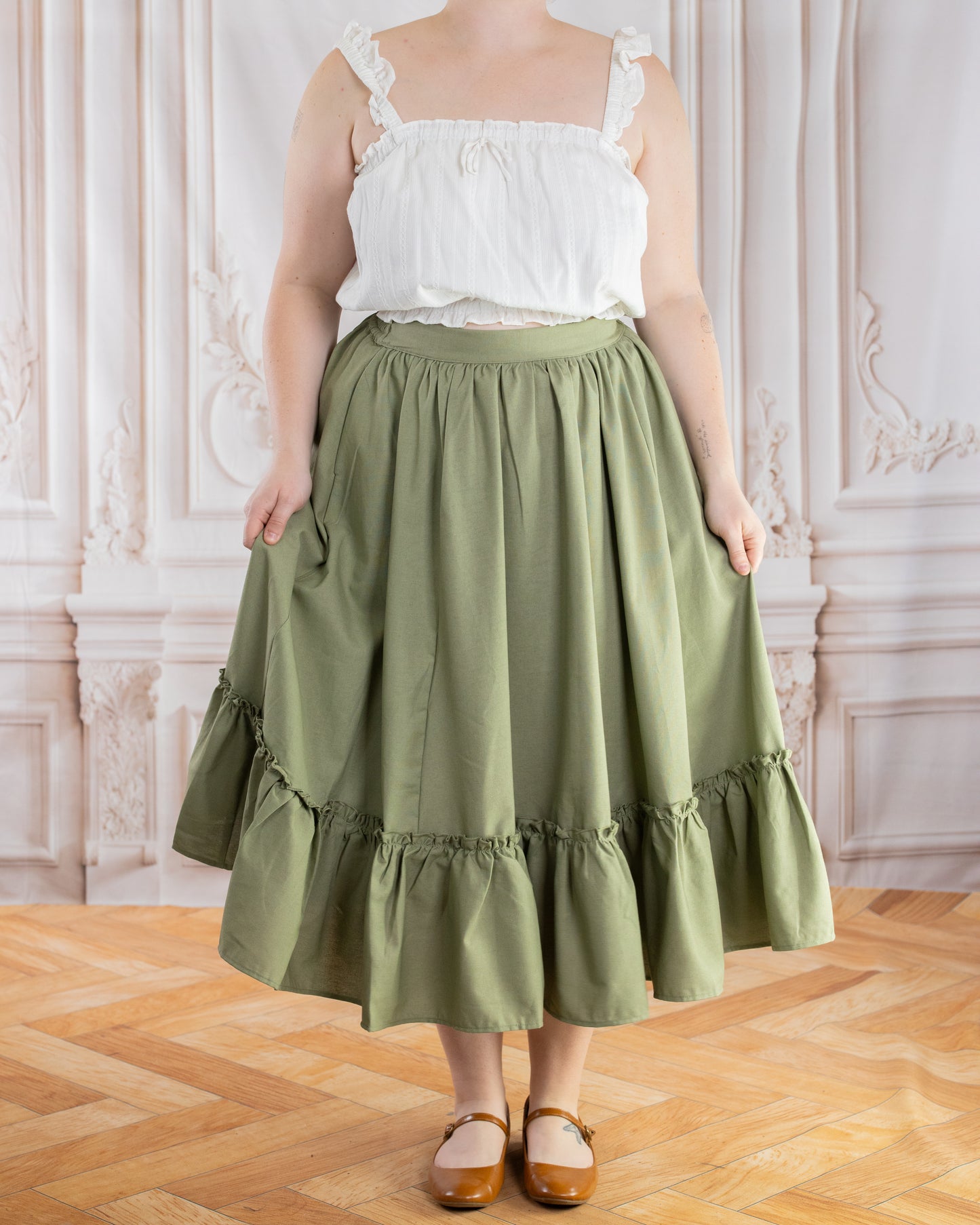 Woman wearing a Sage Linen Ruffle Skirt in sage green with a gathered ruffle hem standing indoors on wood floor