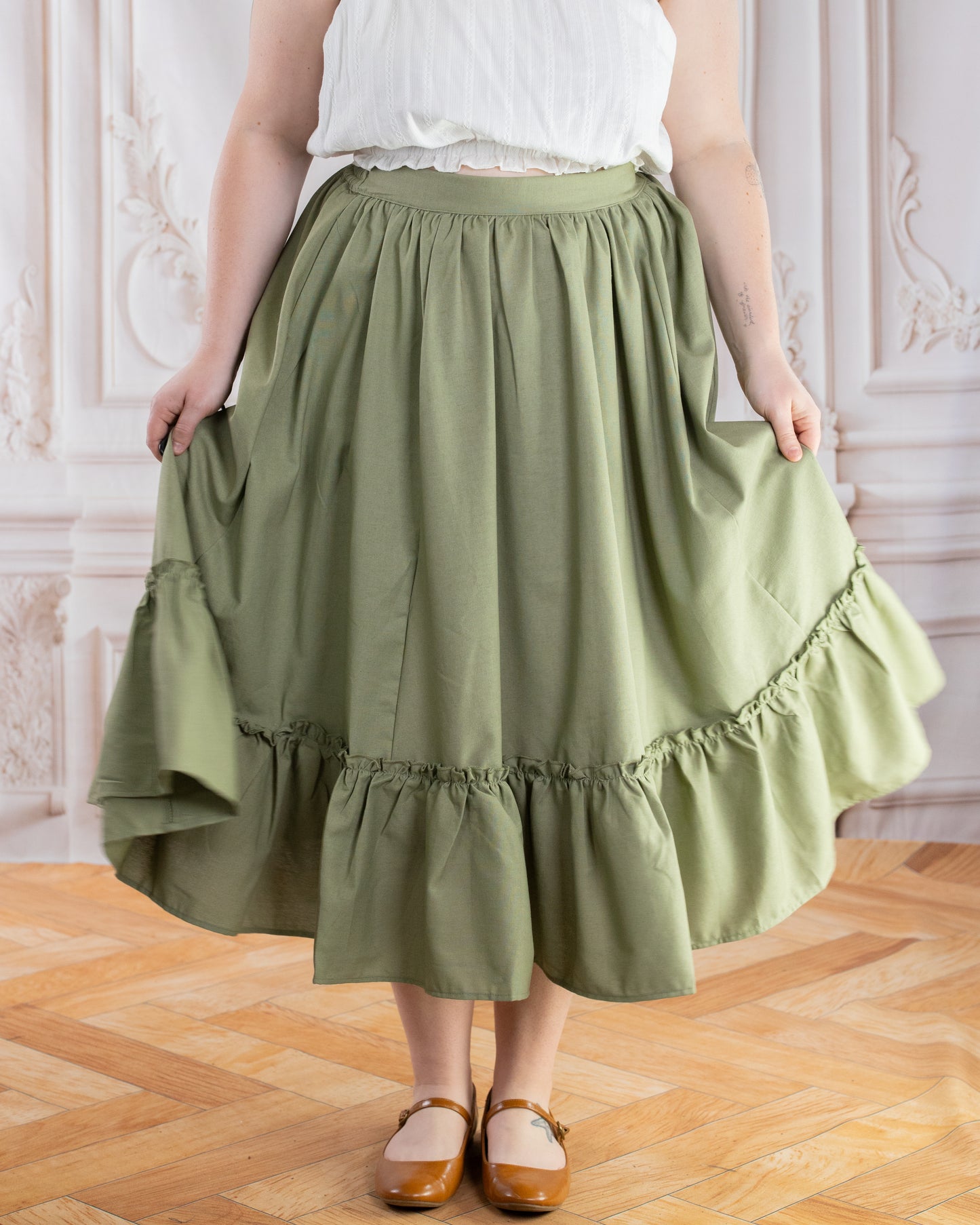 Woman wearing a Sage Linen Ruffle Skirt holding the sides to show the fabric and ruffle detail.