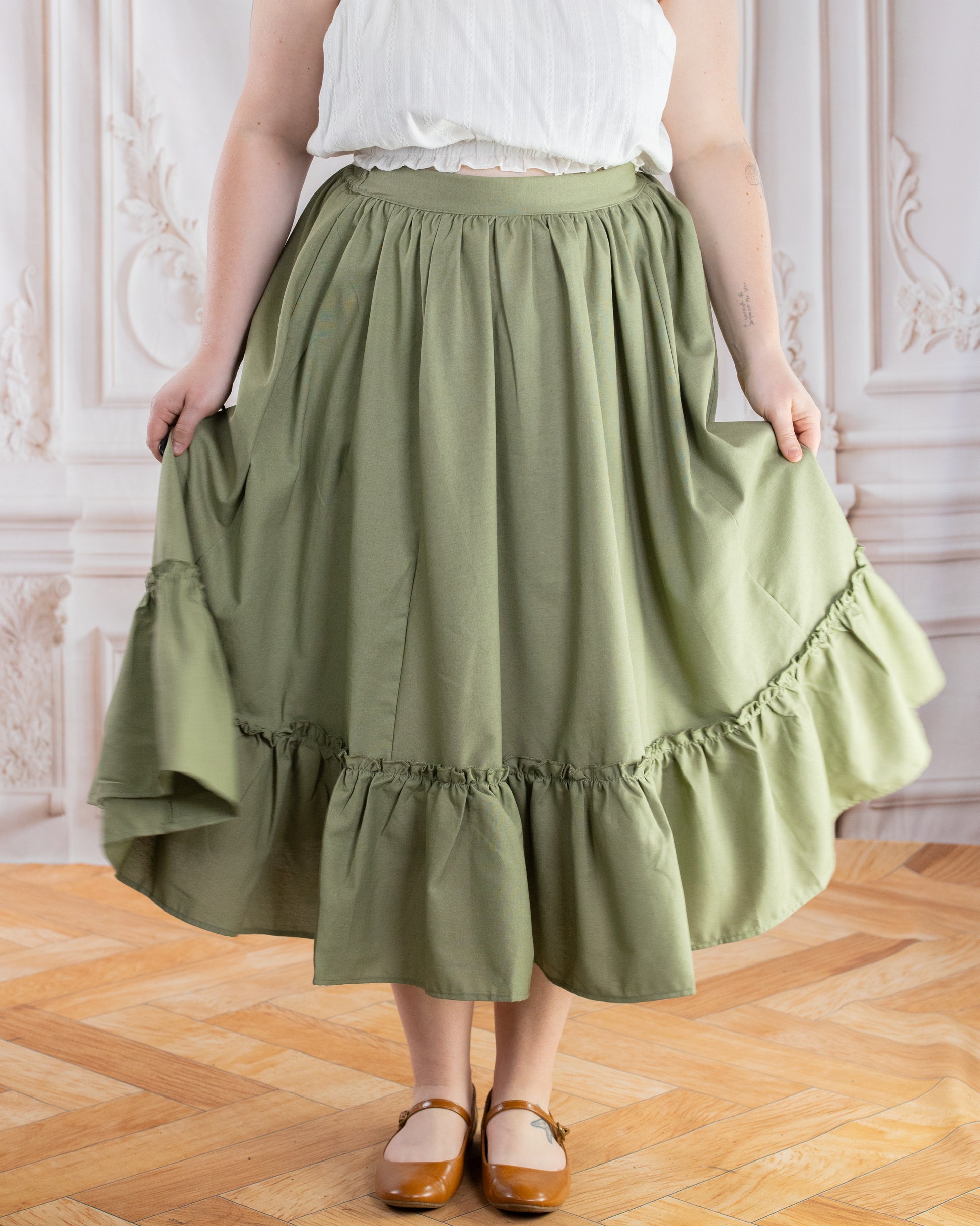Woman wearing a Sage Linen Ruffle Skirt holding the sides to show the fabric and ruffle detail.