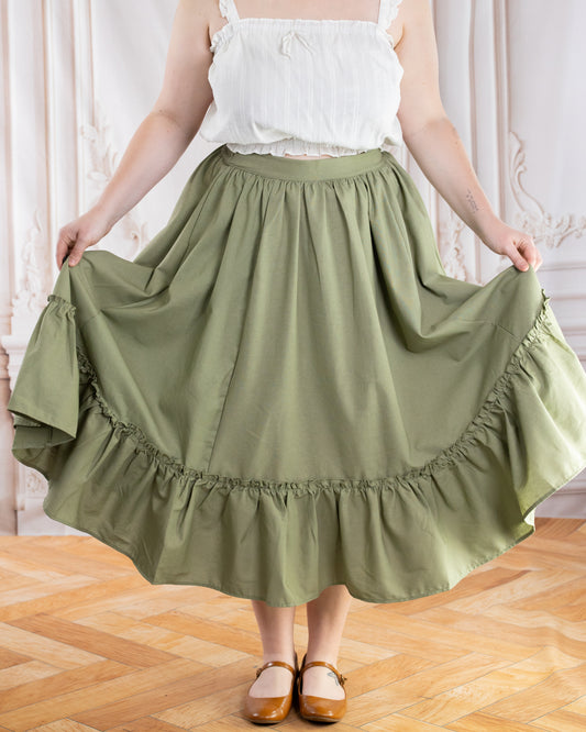 Woman wearing Sage Linen Ruffle Skirt in sage green holding out skirt sides indoors on wooden floor background