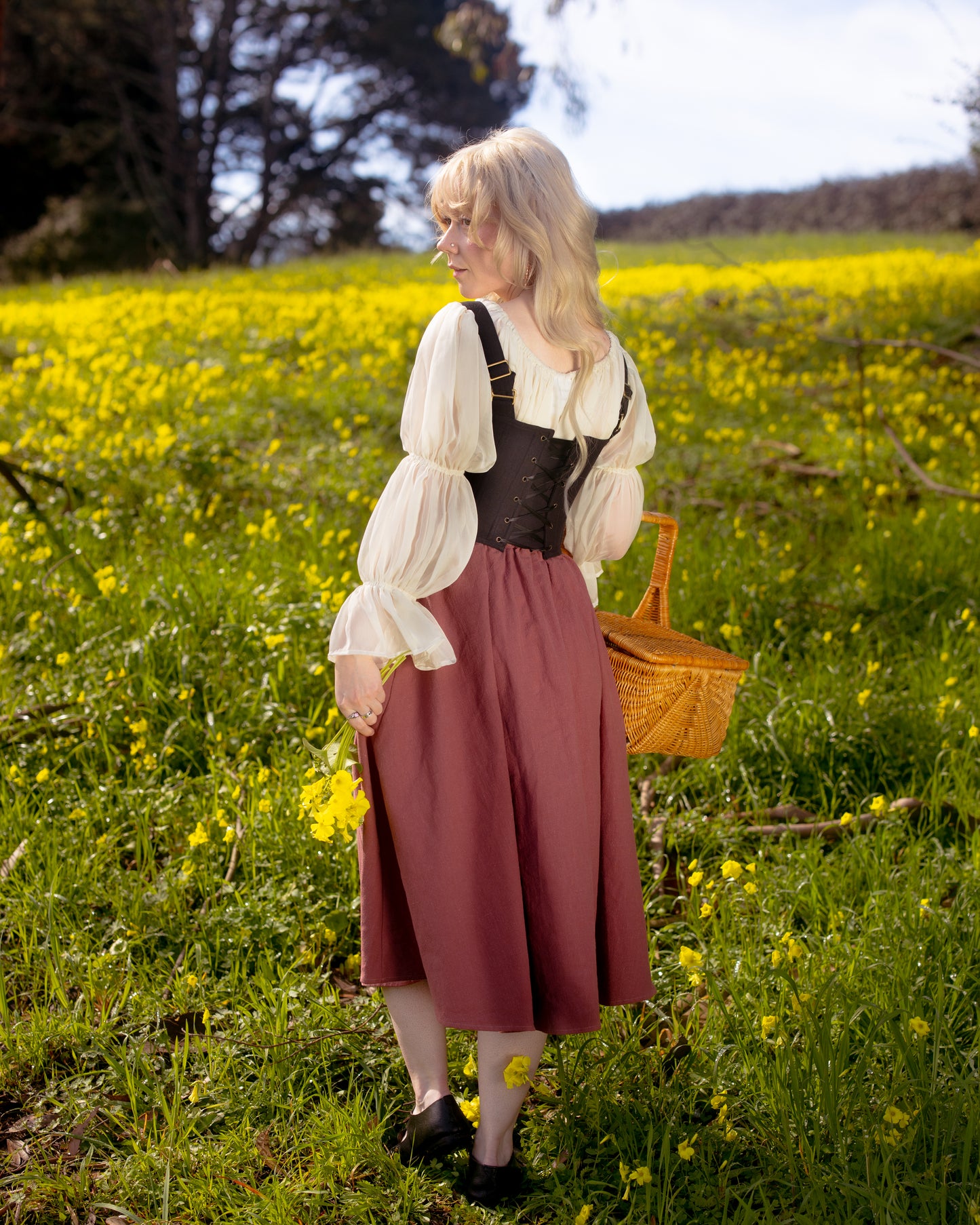 Woman in vintage style black corset and pink skirt holding basket in yellow flower field wearing Black Aurora Stays