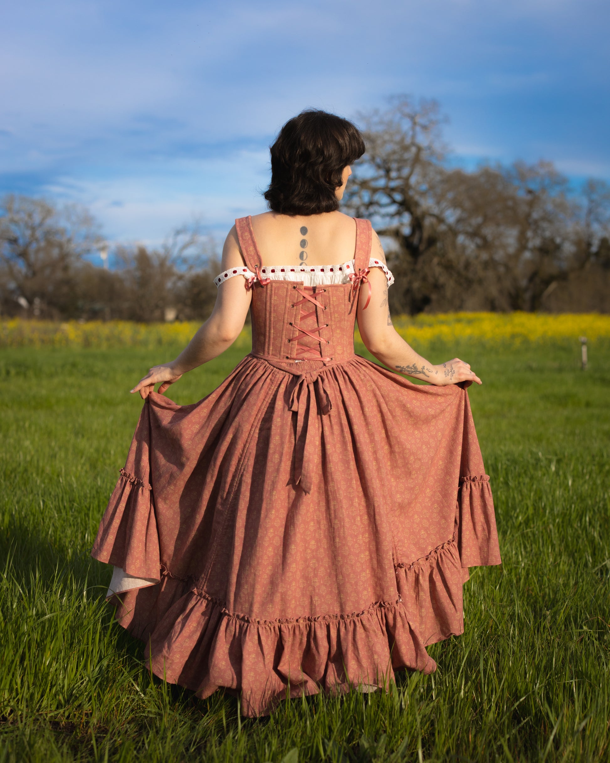 Woman standing in a field wearing a Strawberry Floral Ruffle Skirt with lace-up back and ruffled hem details