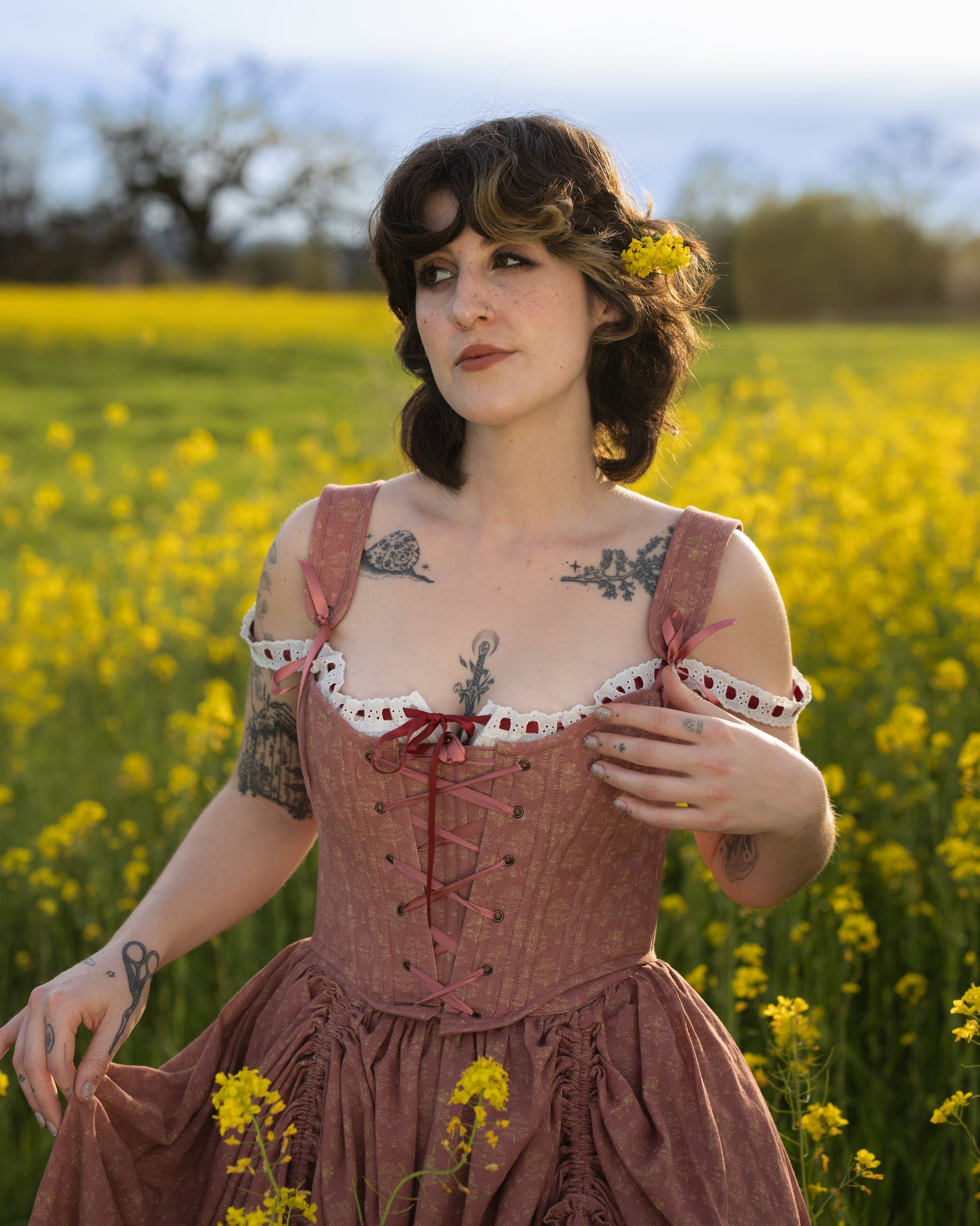 Woman wearing Strawberry Floral Regency Stays dress with lace and ribbons standing in a yellow flower field at sunset