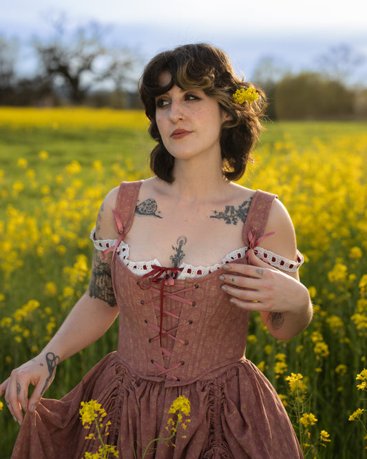 Woman wearing Strawberry Floral Regency Stays dress with lace and ribbons standing in a yellow flower field at sunset
