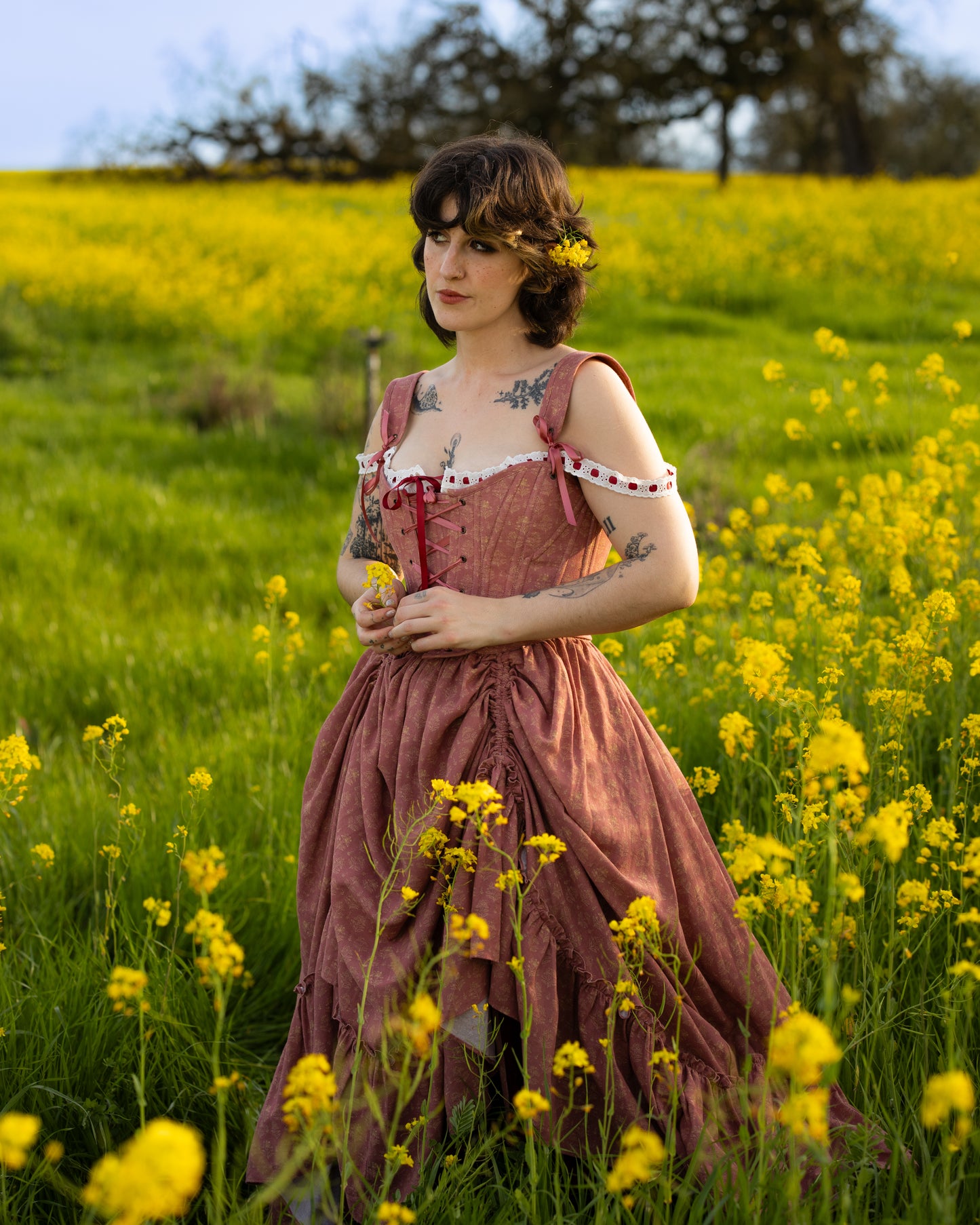 Woman wearing a Strawberry Floral Regency Stays dress standing among yellow wildflowers in a sunlit field