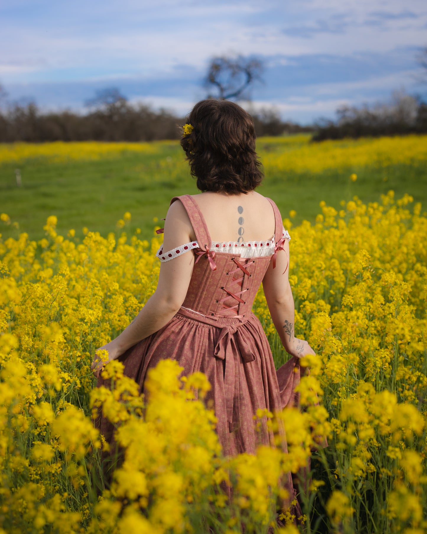 Woman standing in a yellow flower field wearing a Strawberry Floral Regency Stays dress with lace-up back details