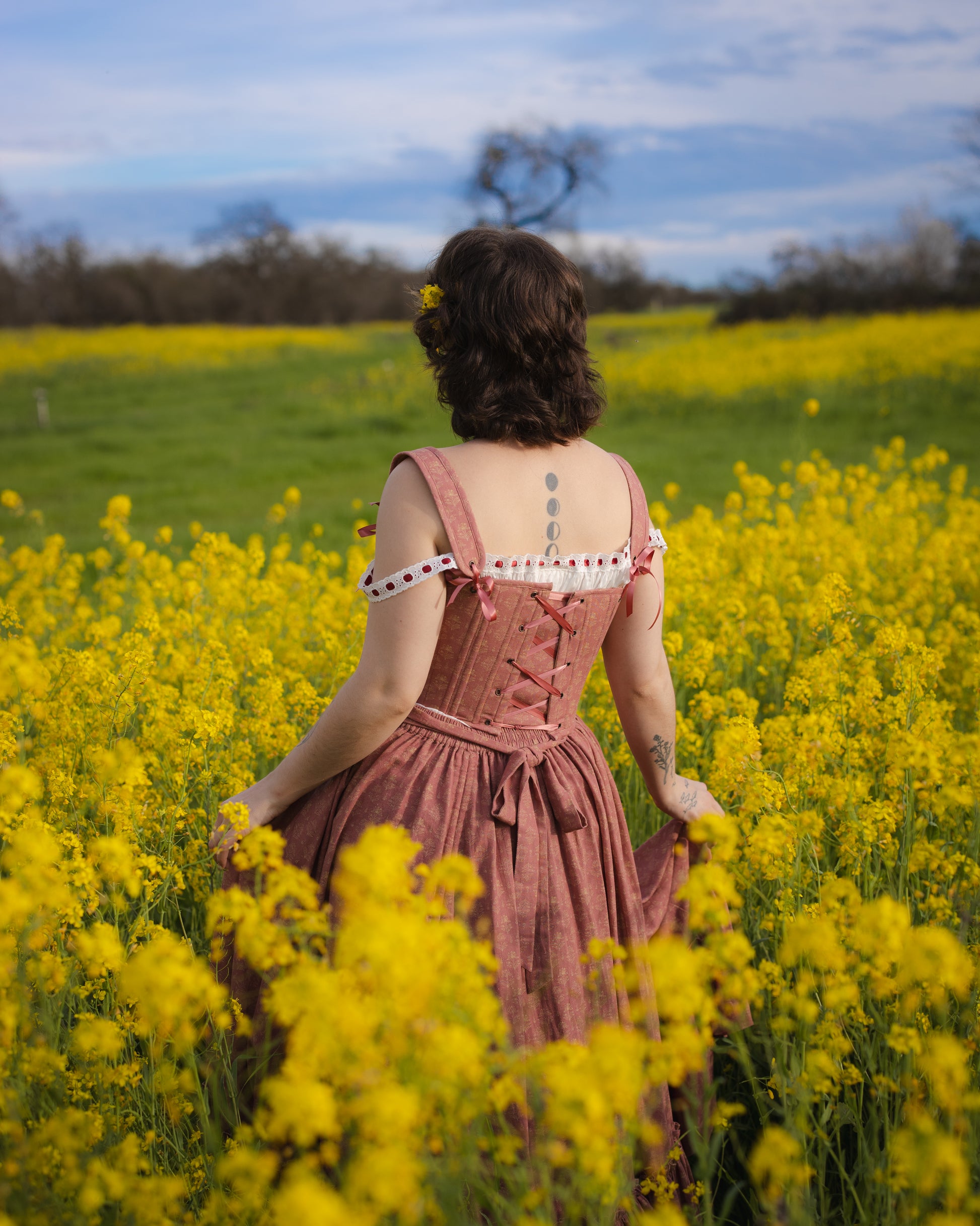 Woman standing in a yellow flower field wearing a Strawberry Floral Regency Stays dress with lace-up back details