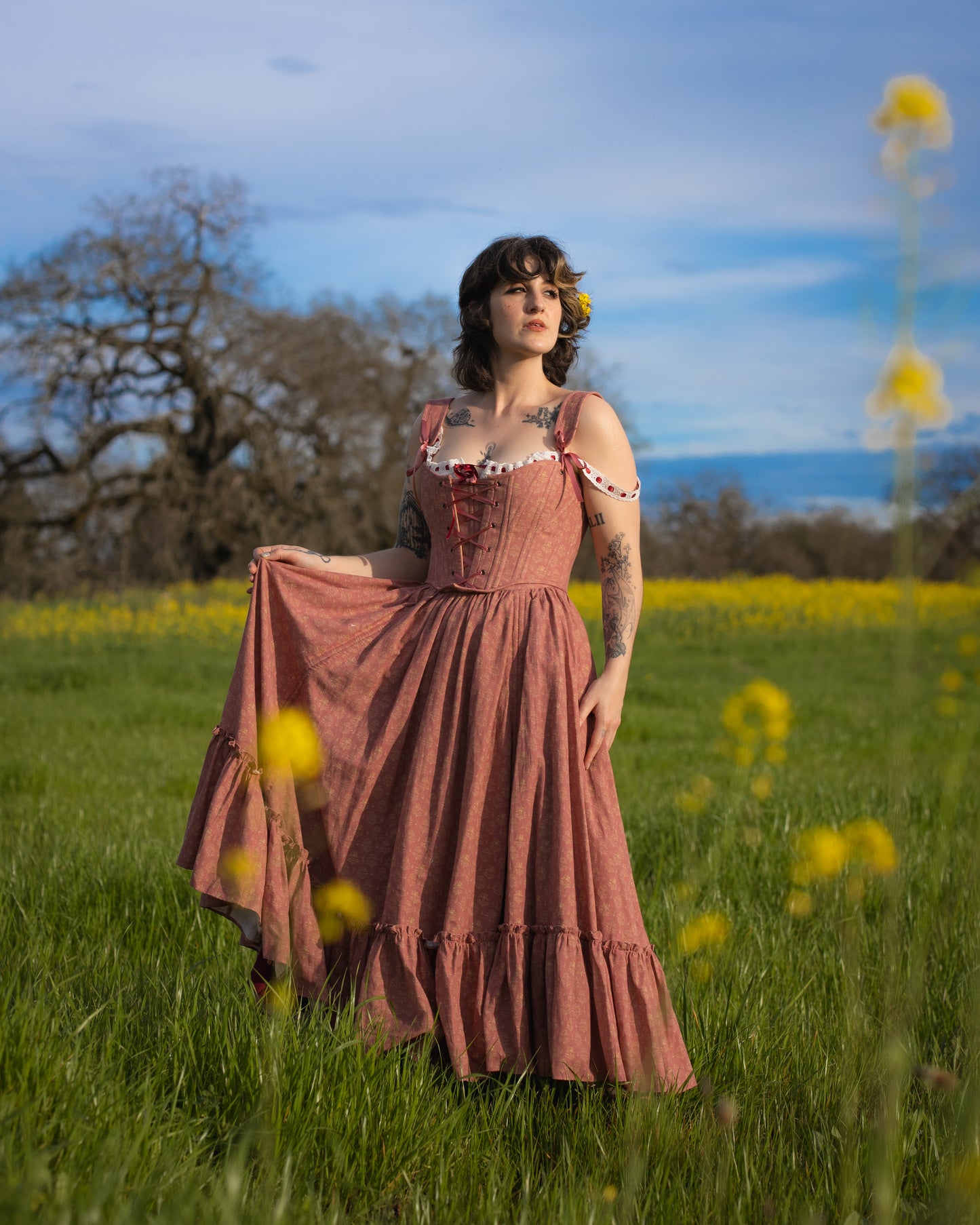 Woman standing in a field wearing a Strawberry Floral Ruffle Skirt with ruffle details and shoulder straps in natural light
