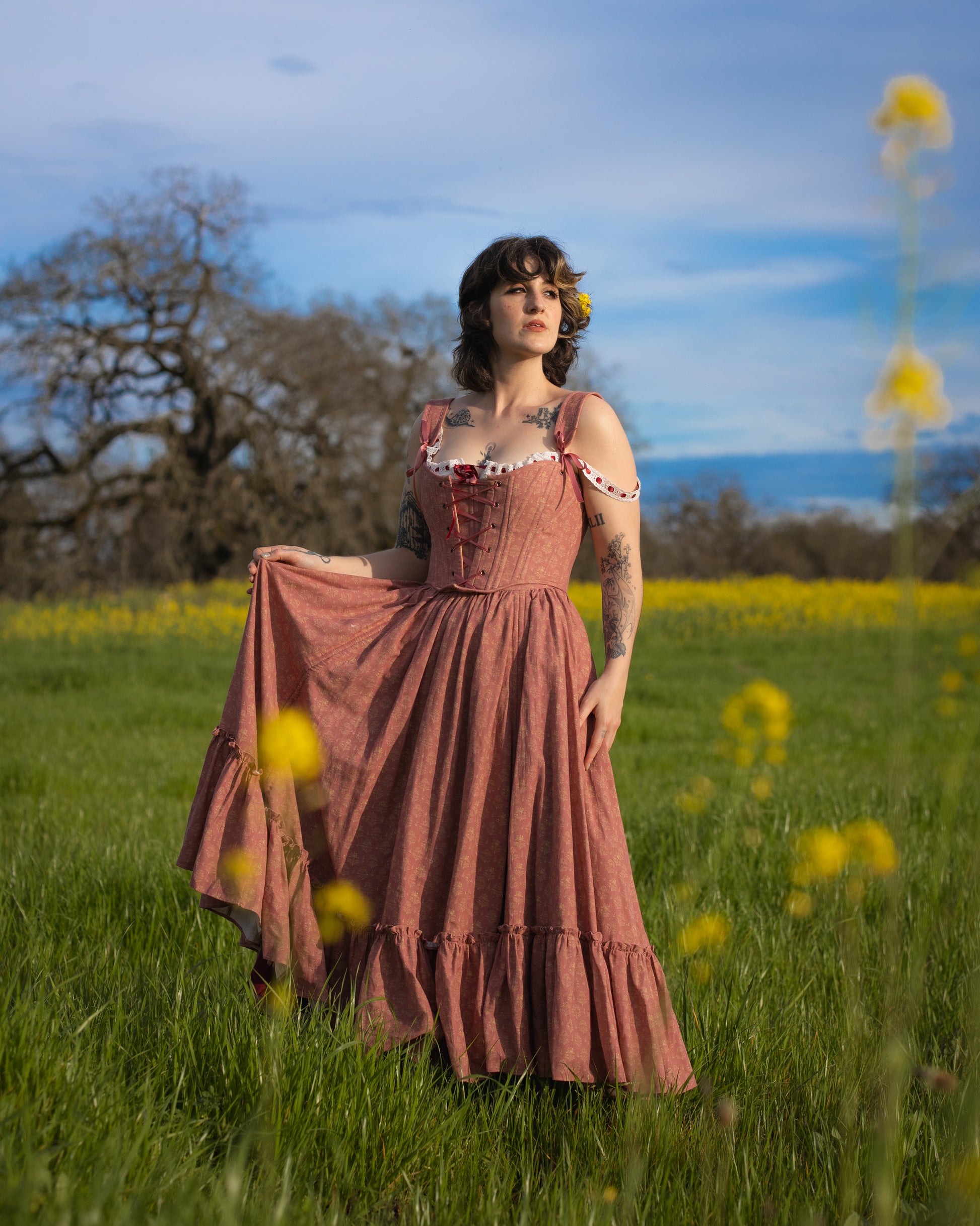Woman standing in a field wearing a Strawberry Floral Ruffle Skirt with ruffle details and shoulder straps in natural light