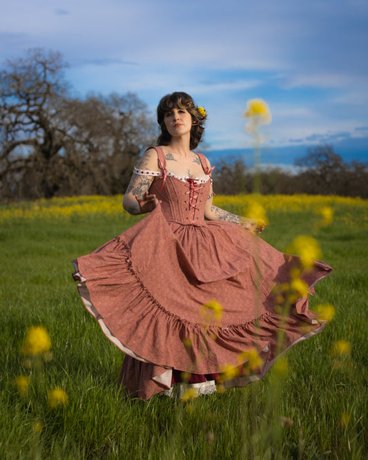 Woman wearing Strawberry Floral Regency Stays dress twirling in a green field with yellow flowers under a blue sky