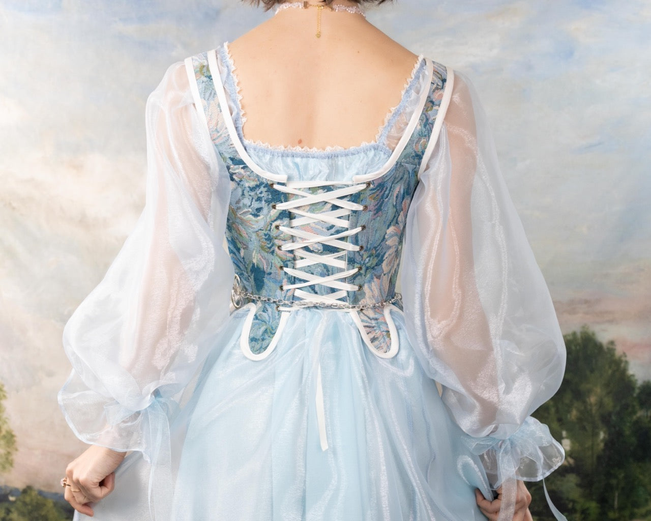Back view of a woman wearing Handmade Teal Floral Tapestry 18th Century Stays with sheer puff sleeves over a light blue dress