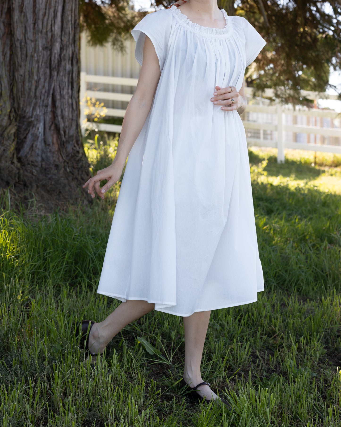 Woman outdoors wearing white Cotton Flutter Sleeve Chemise with elastic neckline in natural light and grassy setting