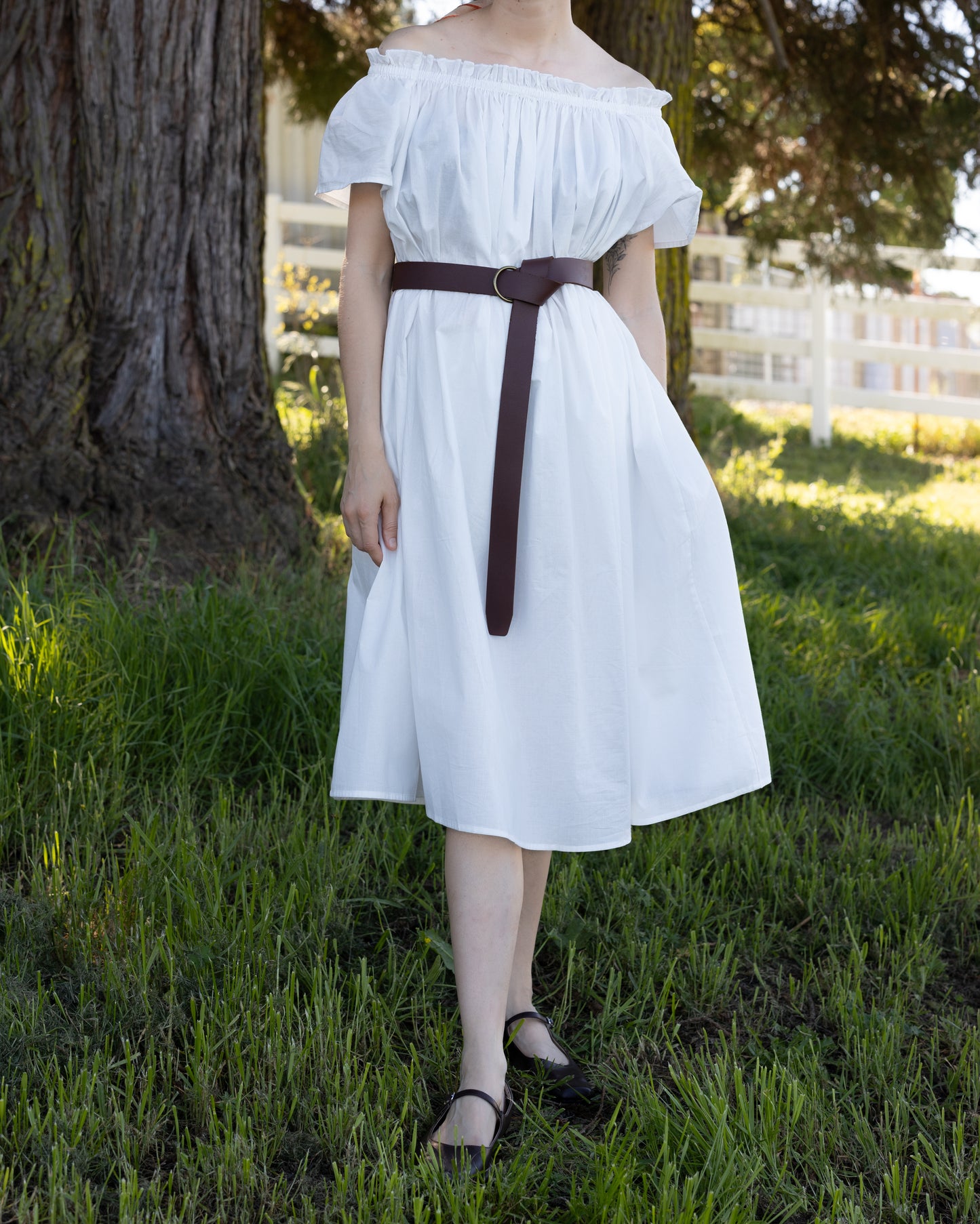 Woman in white Cotton Flutter Sleeve Chemise with elastic neckline and brown belt standing in grassy outdoor setting
