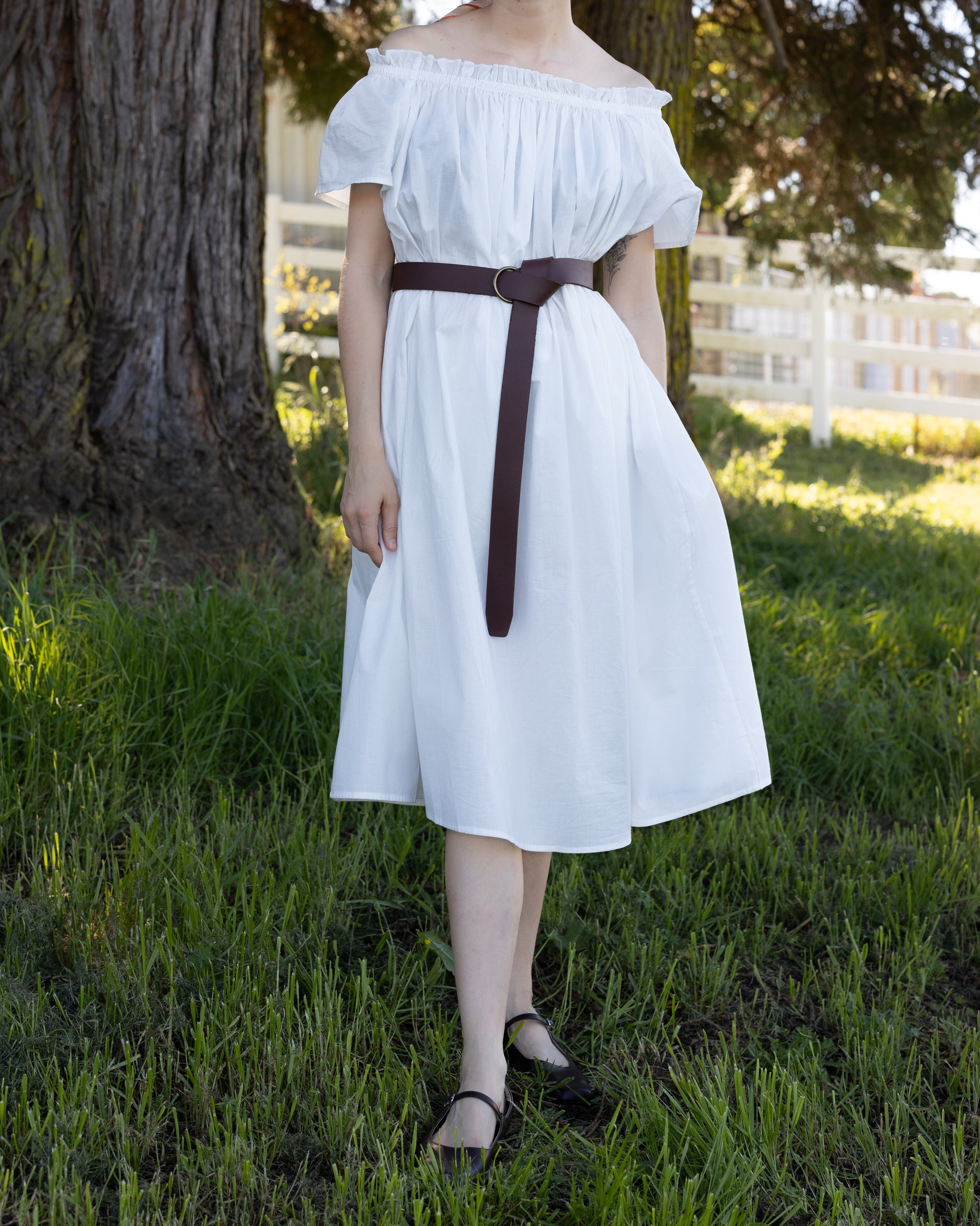 Woman in white Cotton Flutter Sleeve Chemise with elastic neckline and brown belt standing in grassy outdoor setting